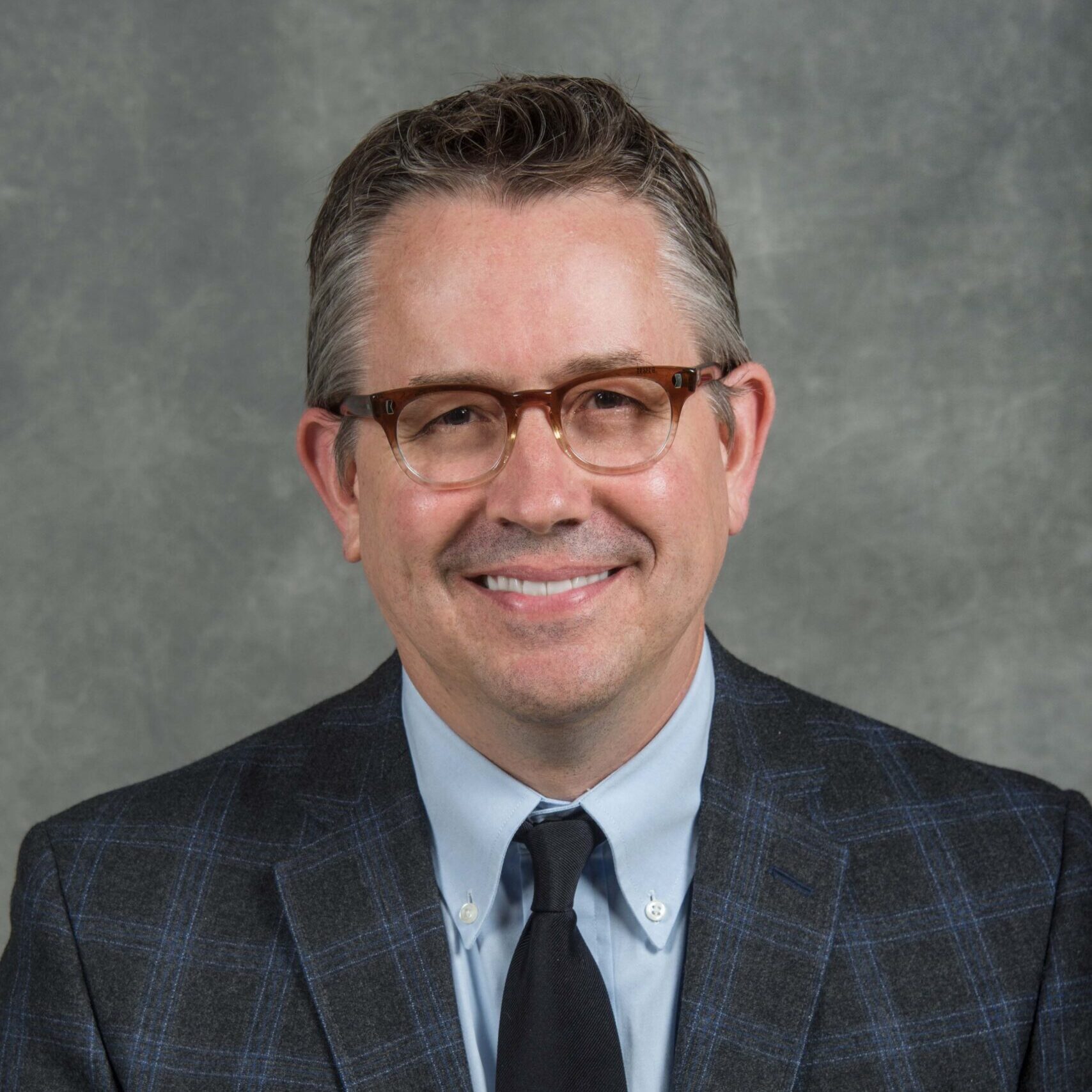 Brown-eyed person with glasses wearing a blue plaid suit.