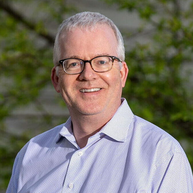 Gray-haired person in glasses wearing a purple shirt.