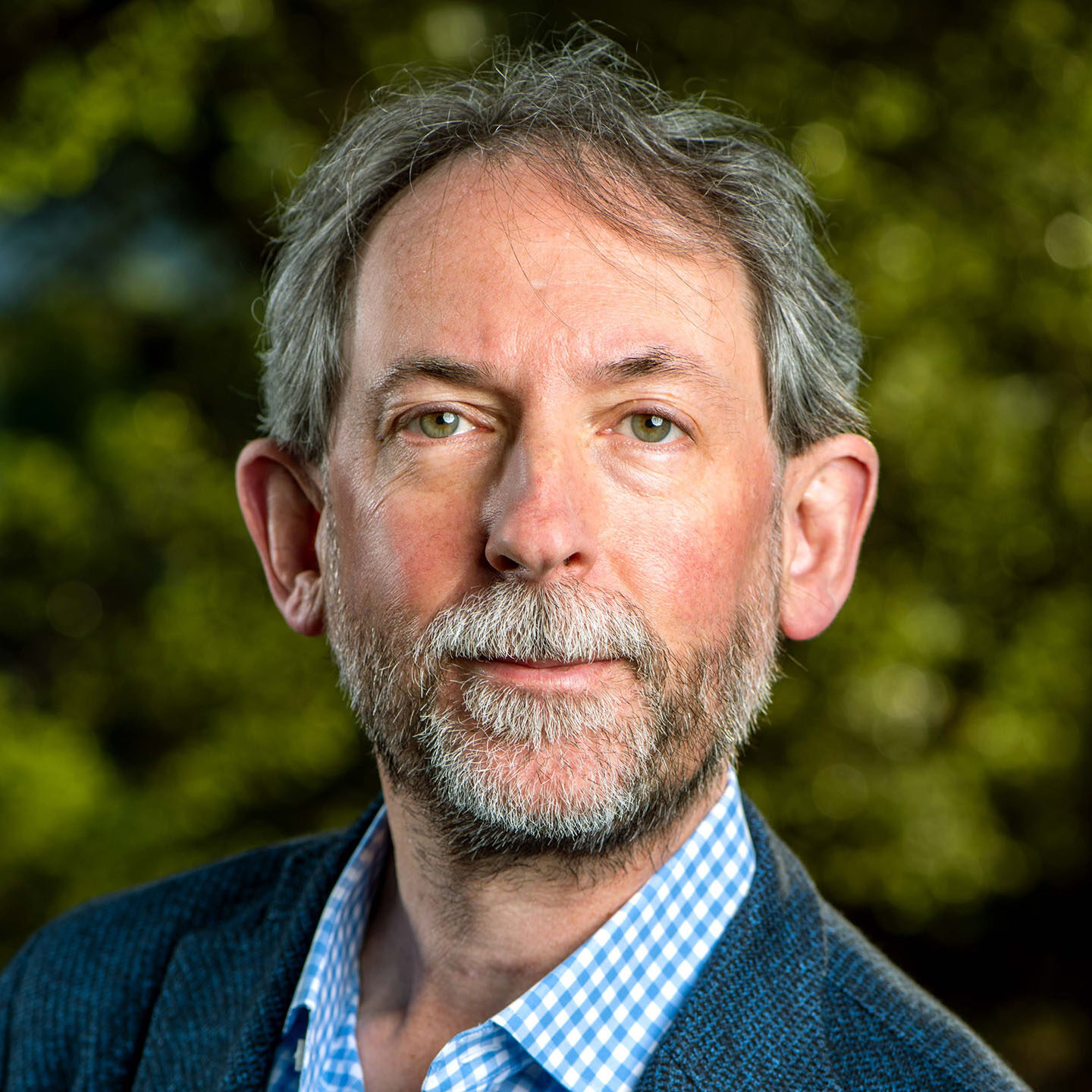 Grey-haired person with green eyes wearing a blue suit.