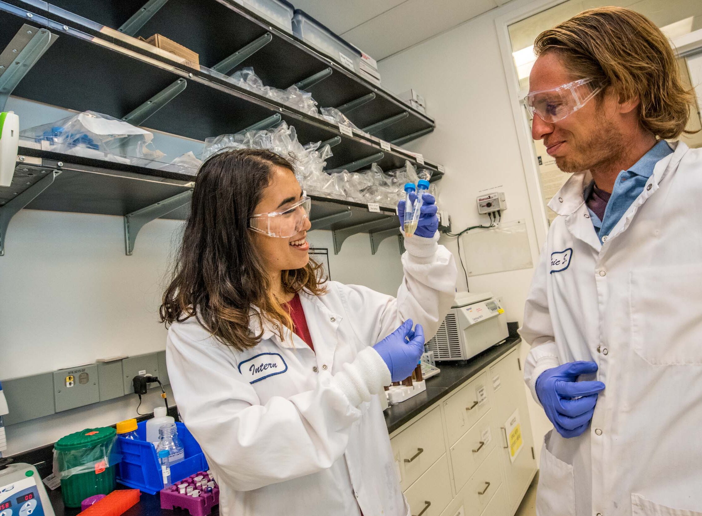 One scientist holding two vials next to another scientist.