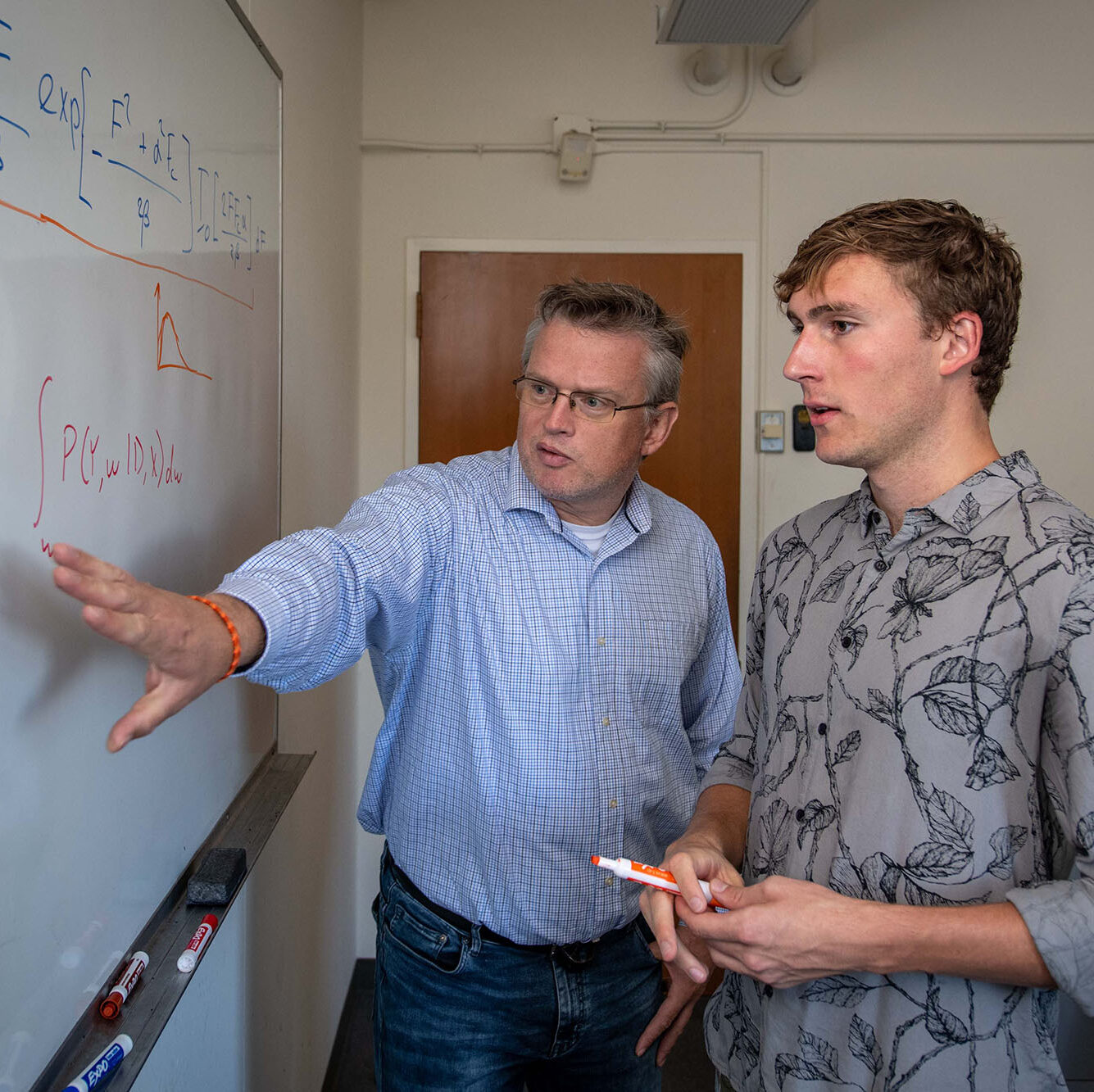 Two people staring and pointing at a whiteboard with scientific equations.