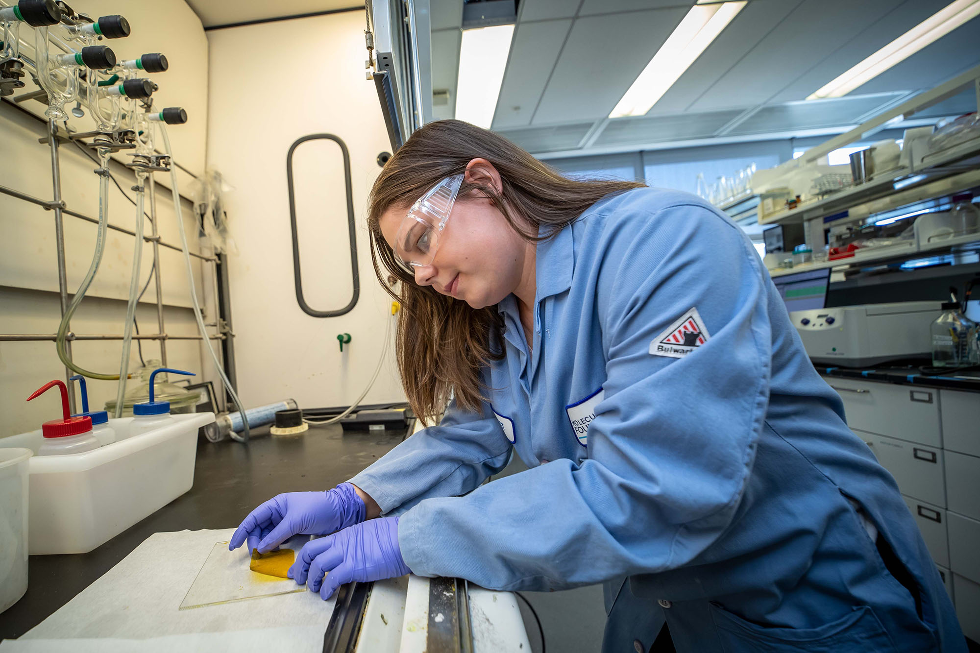 A scientist in a blue lab coat handles a material.