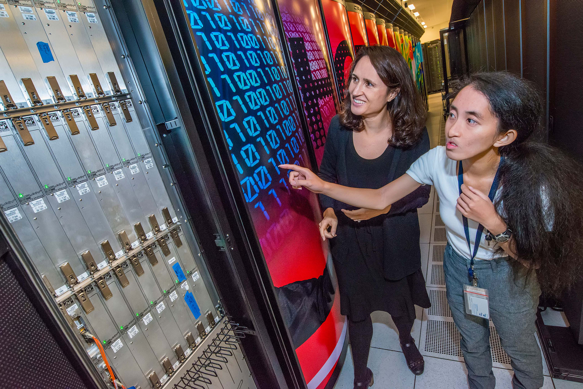 Two dark-haired people standing next to a high-performance super computer.