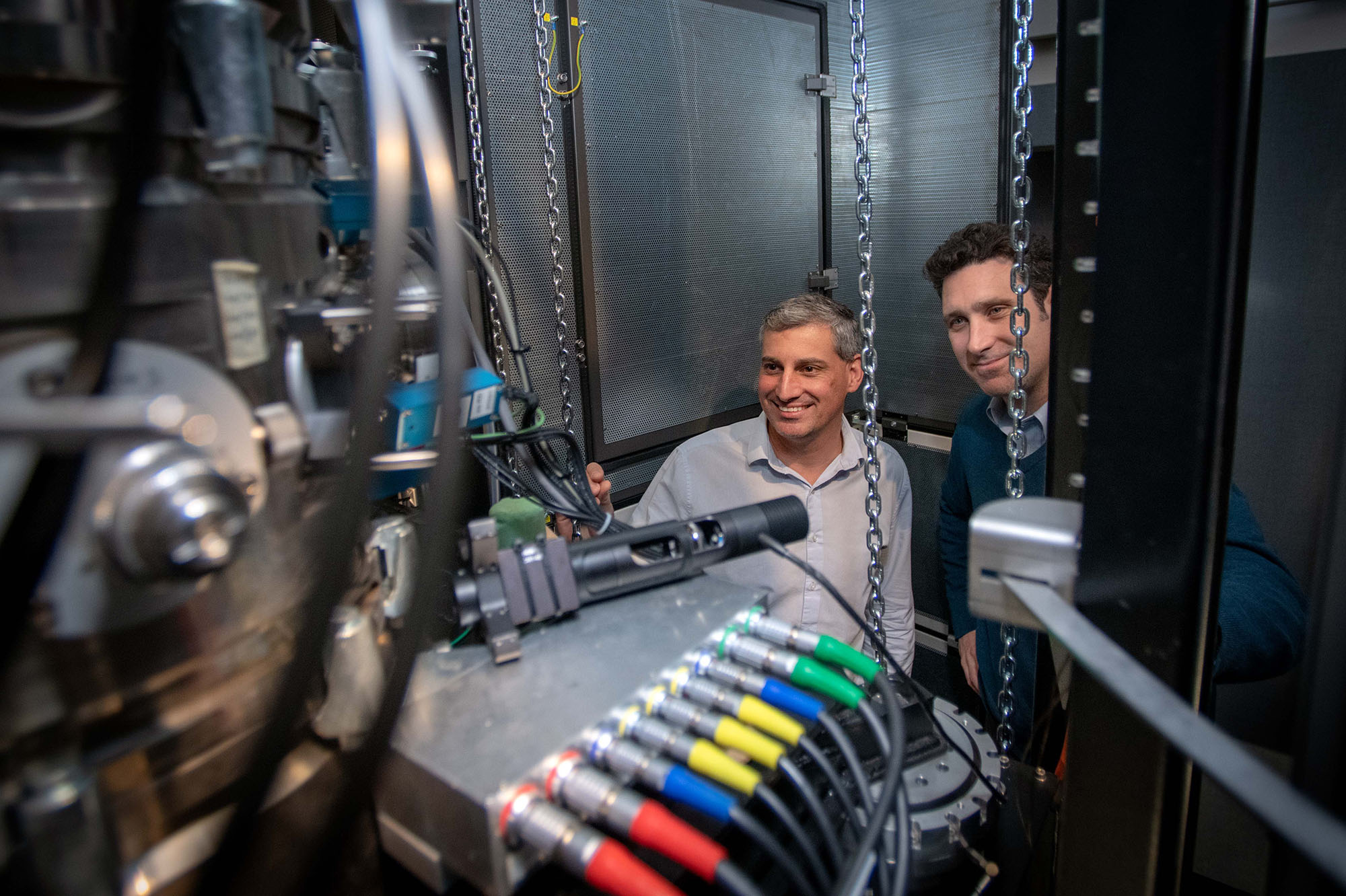 Two researchers stand facing a microscopic detector.