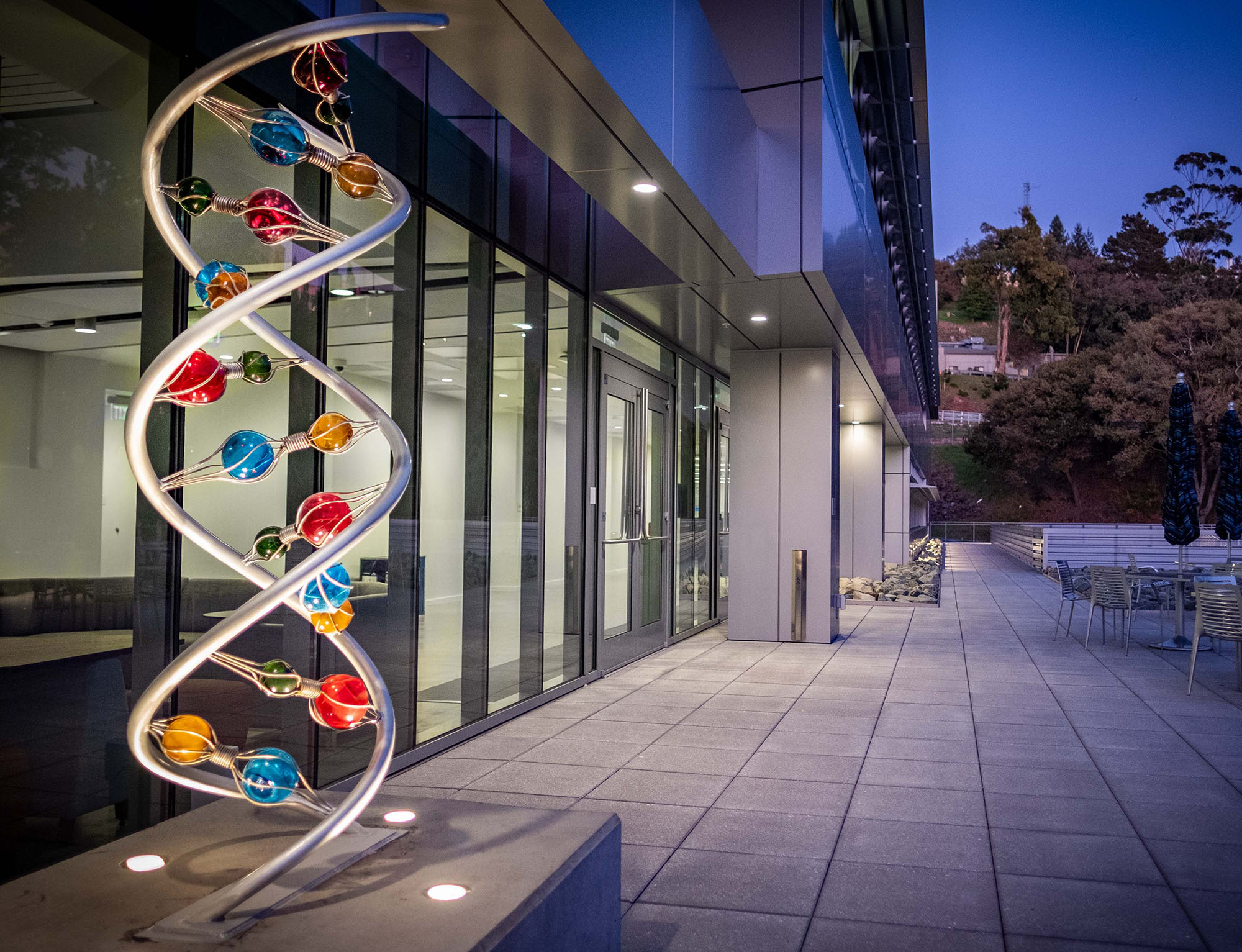 A color sculpture of helix DNA in front of a dusk-bathed building.