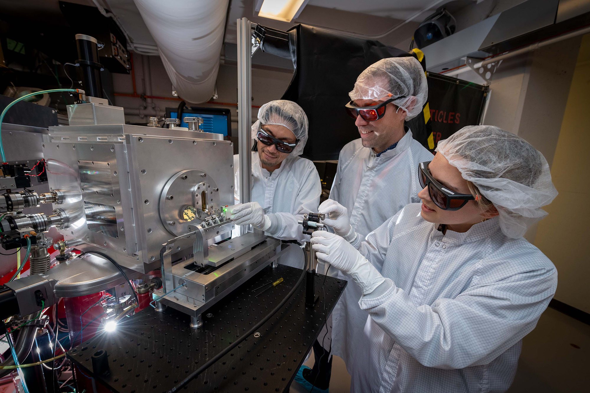 Three scientists in protective gear inspecting a table-top laser.