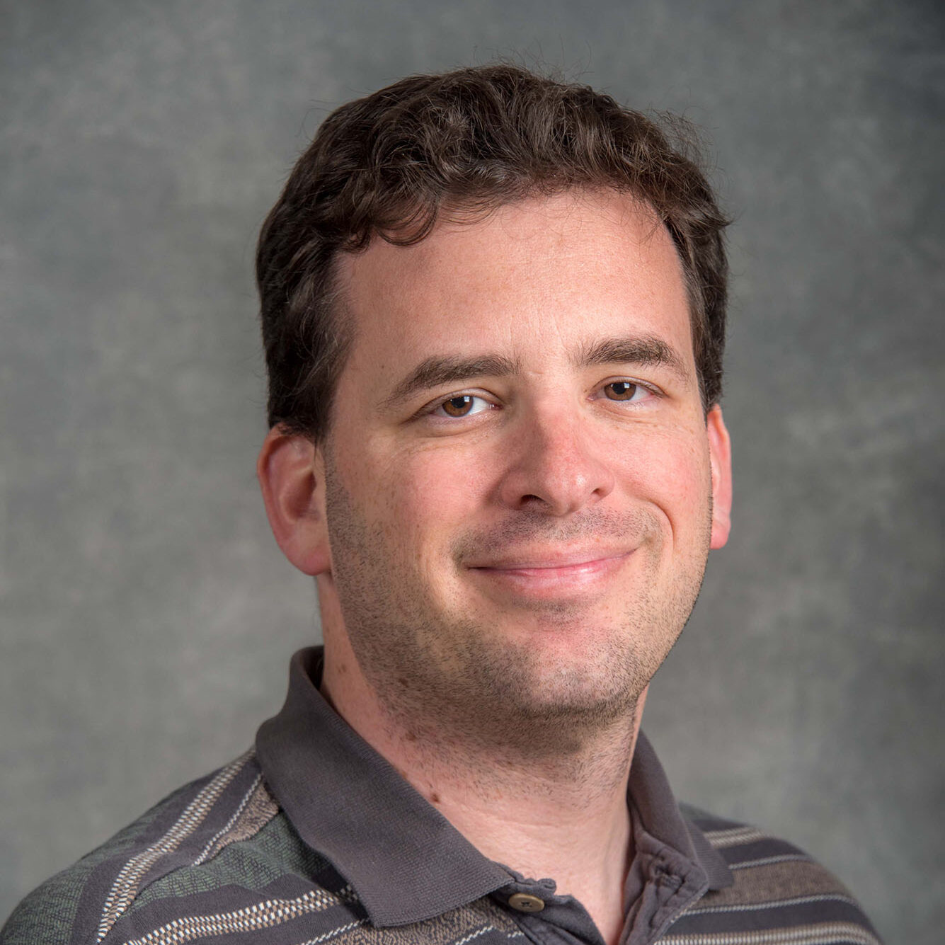 Dark-haired person wearing a polo in front of a photo screen.