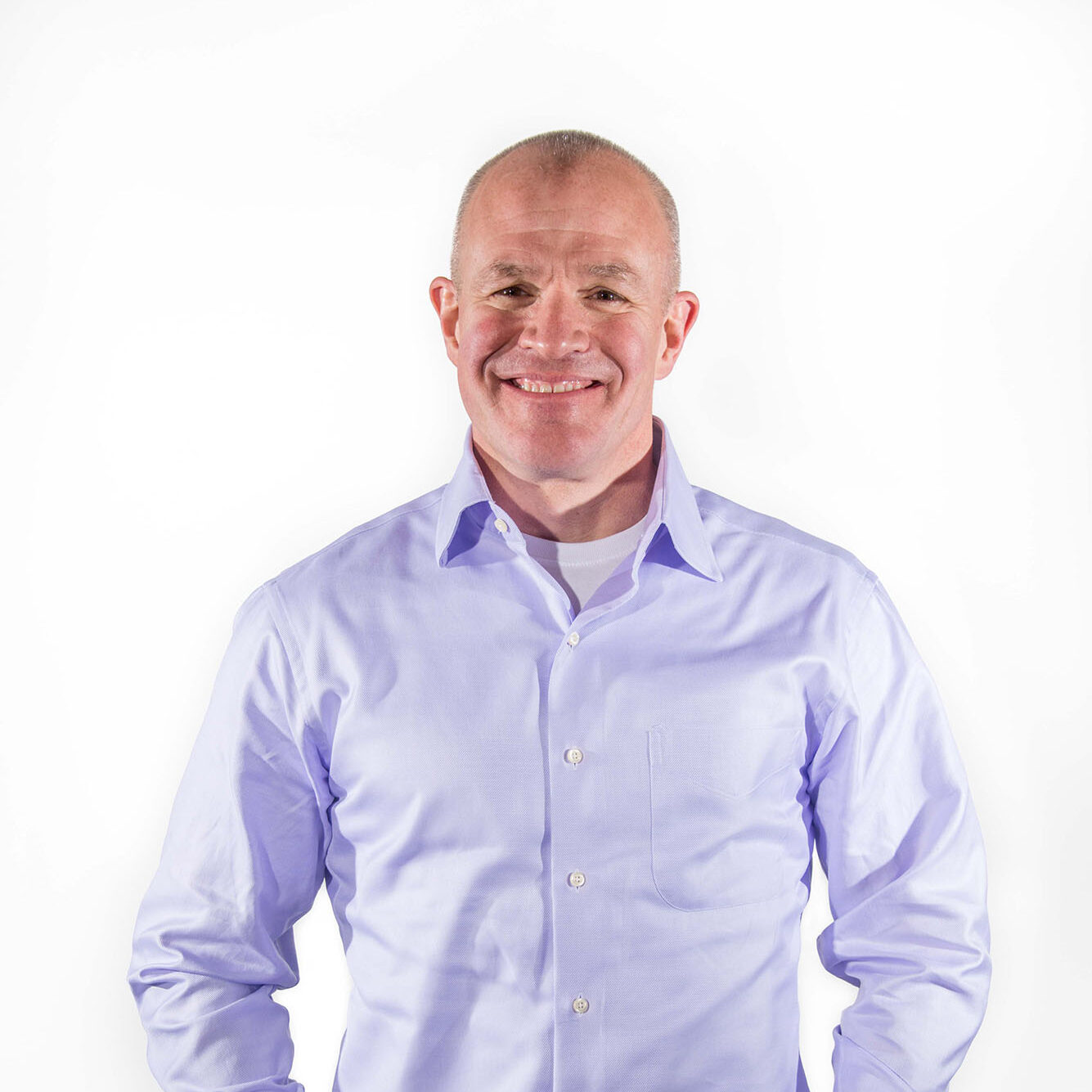 Short-haired person wearing a purple shirt standing in front of a white wall.