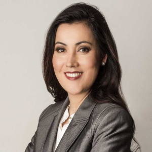 Daniela Ushizima, a dark-haired person wearing a gray jacket, smiles against a light gray background.