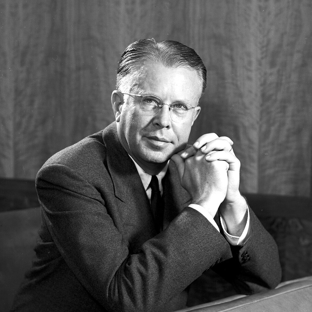 Short-haired person with glasses in a suit.