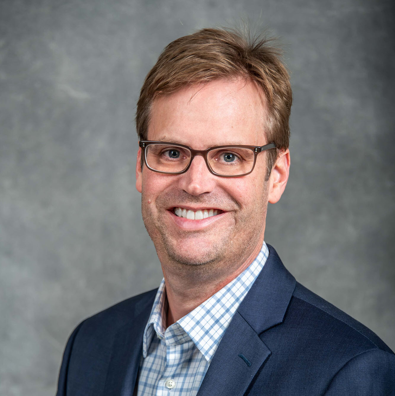 Blonde-haired person with glasses wearing a navy suit.