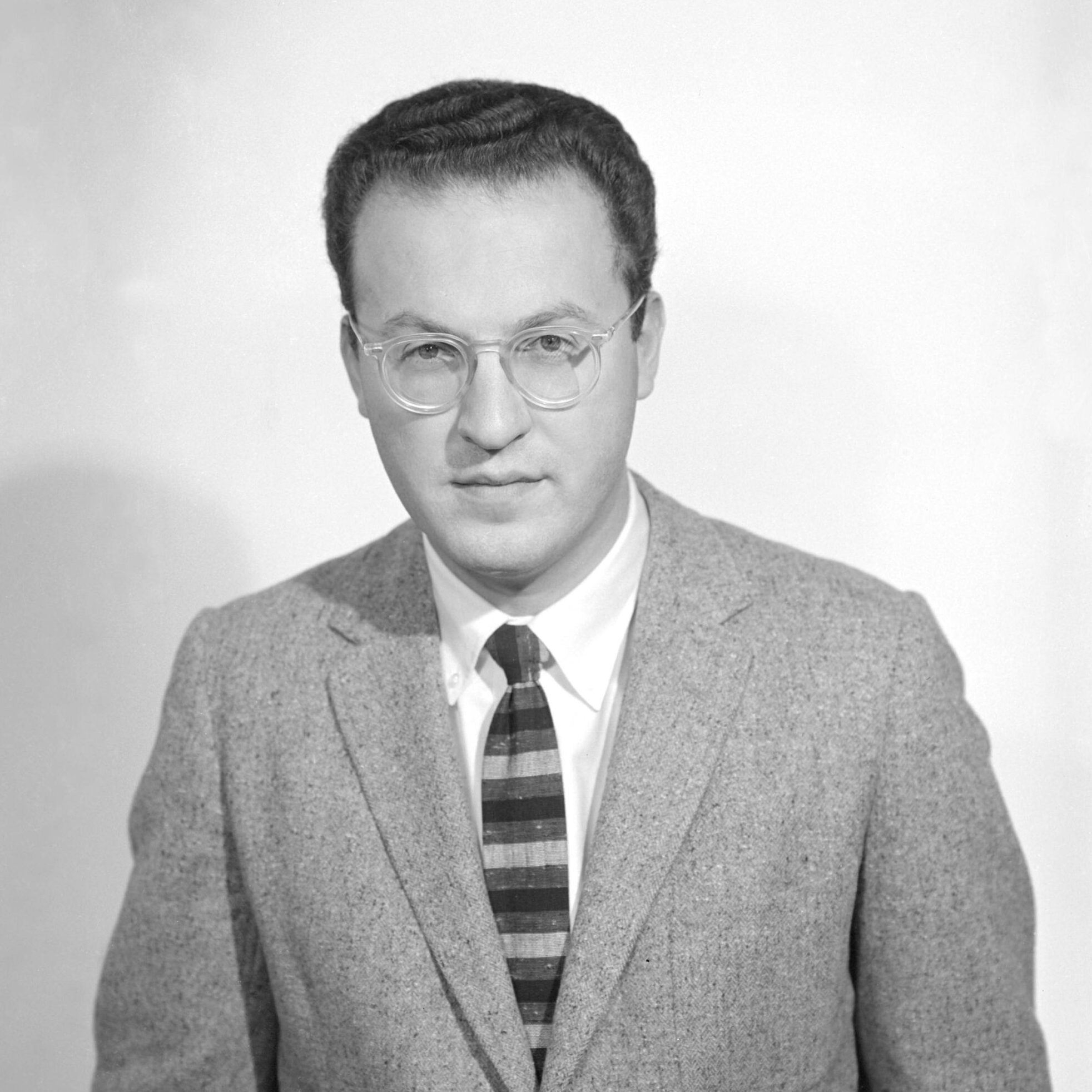 Dark-haired person with glasses in a suit and tie.