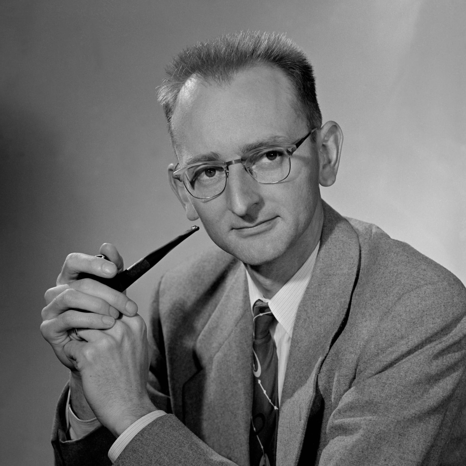 Short-haired person in glasses holding a smoking pipe.