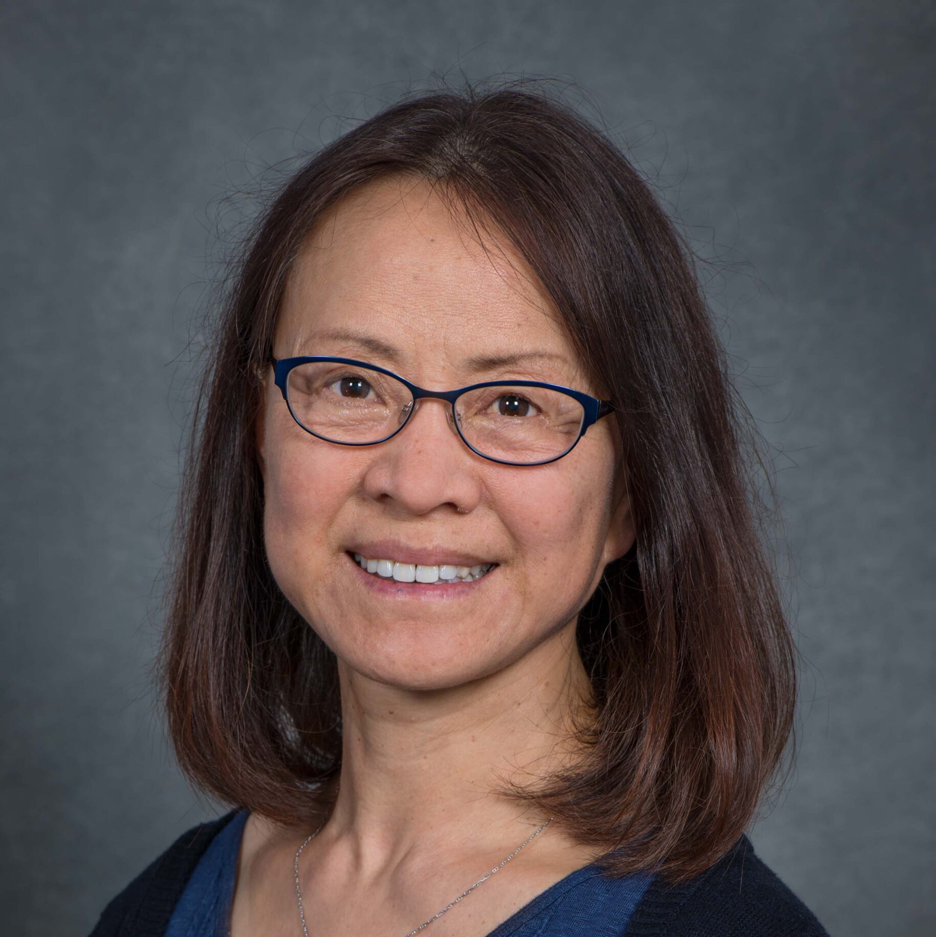 Dark-haired person with glasses wearing a blue blouse.