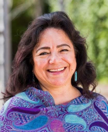Dark-haired person wearing a purple and teal patterned blouse.