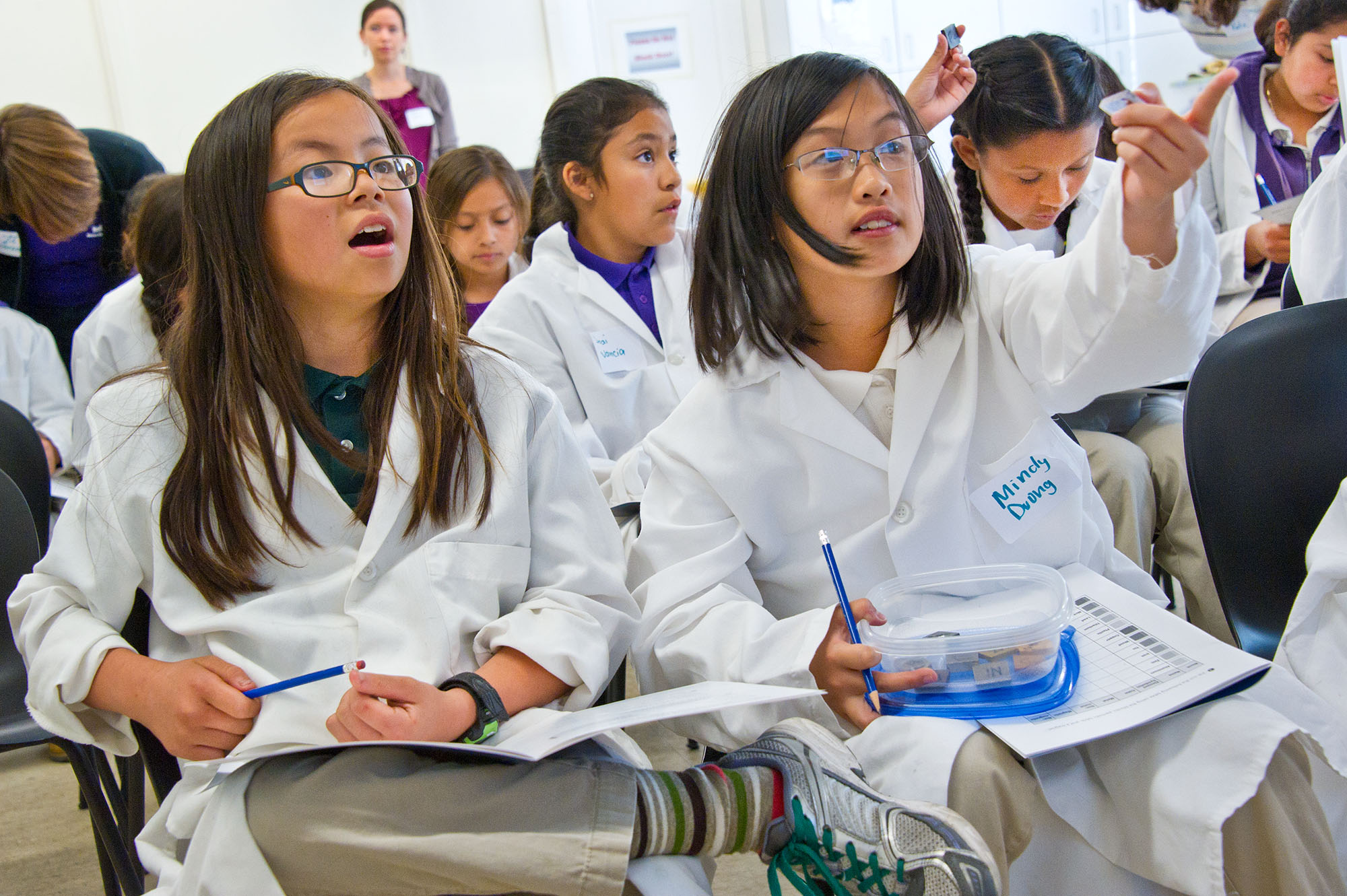 Students in lab coats listen to a presentation.