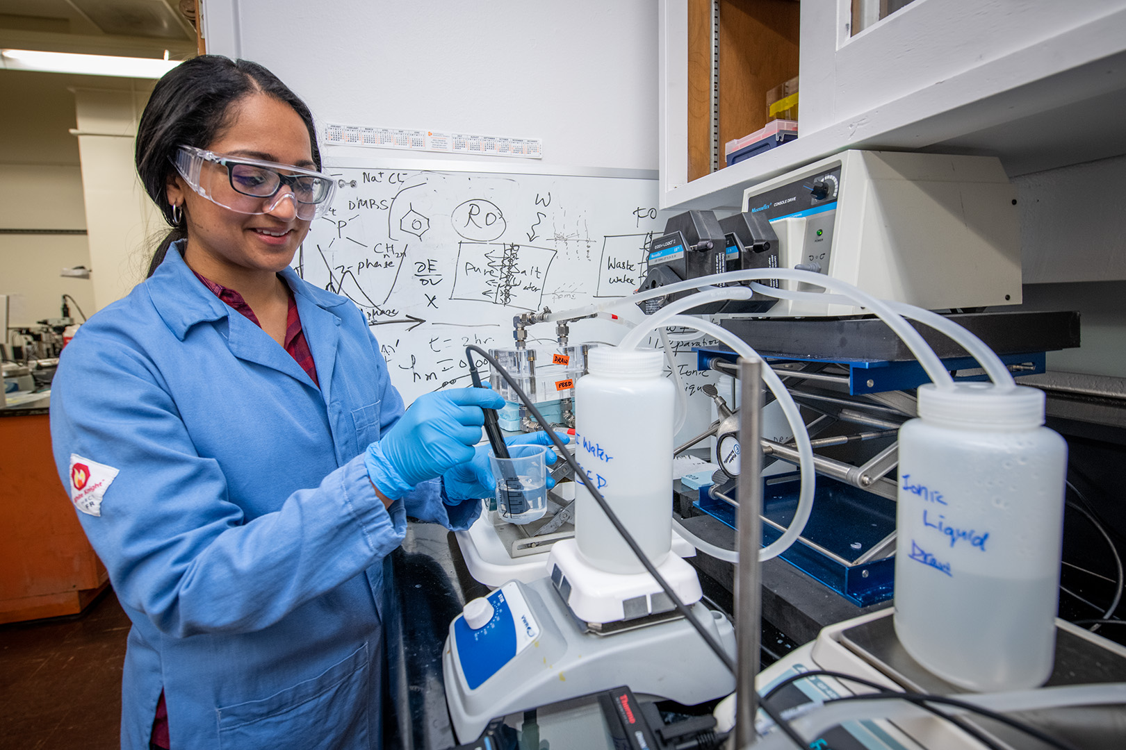 Scientist wearing goggles operates a small desalination experiment at a lab bench.