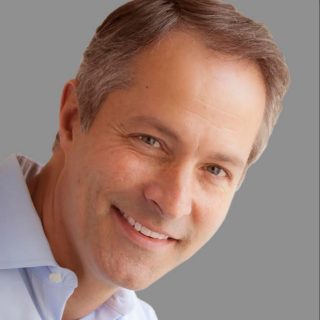 Peter Fiske, a short-haired person wearing a collared shirt, smiles for a headshot against a gray background.