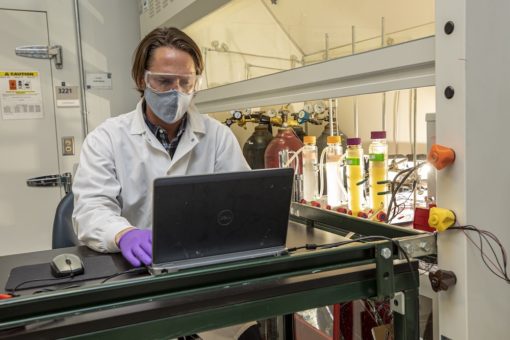 Scientist at a lab bench working on a laptop.