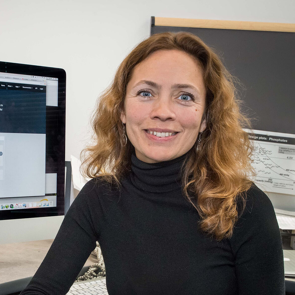 Kristin Persson, a brown-haired person wearing a black turtleneck, smiles at her desk.