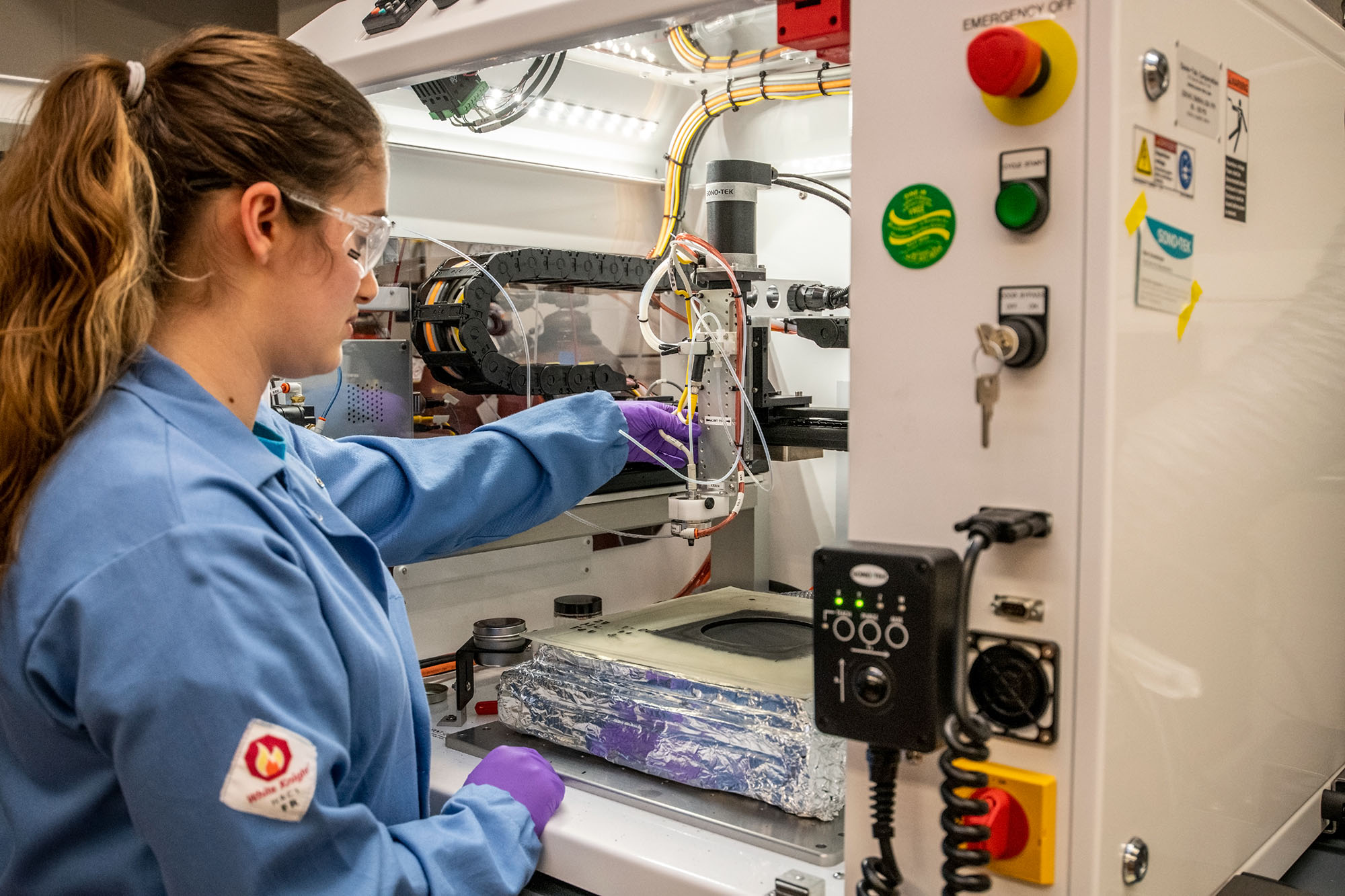 Scientist in a blue lab coat conducting experiments in a large open machine.