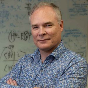 Light-haired person in a blue shirt standing in front of a whiteboard.