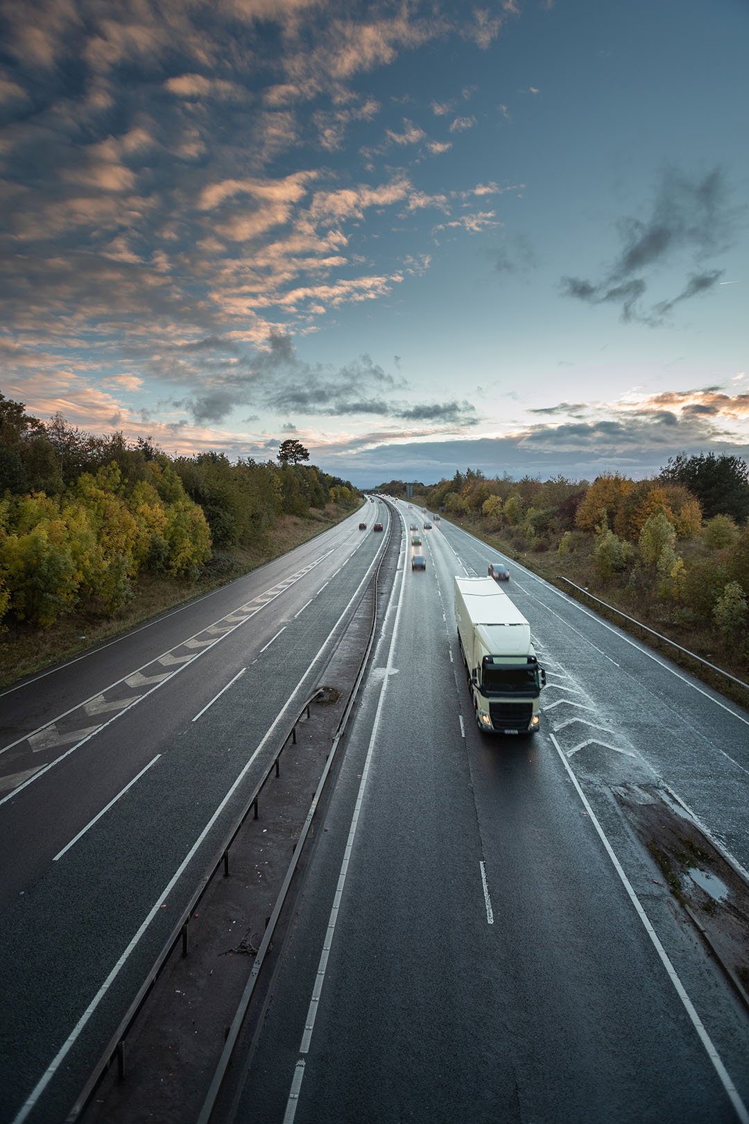 View of highway at sunrise with a semi coming toward the viewer.