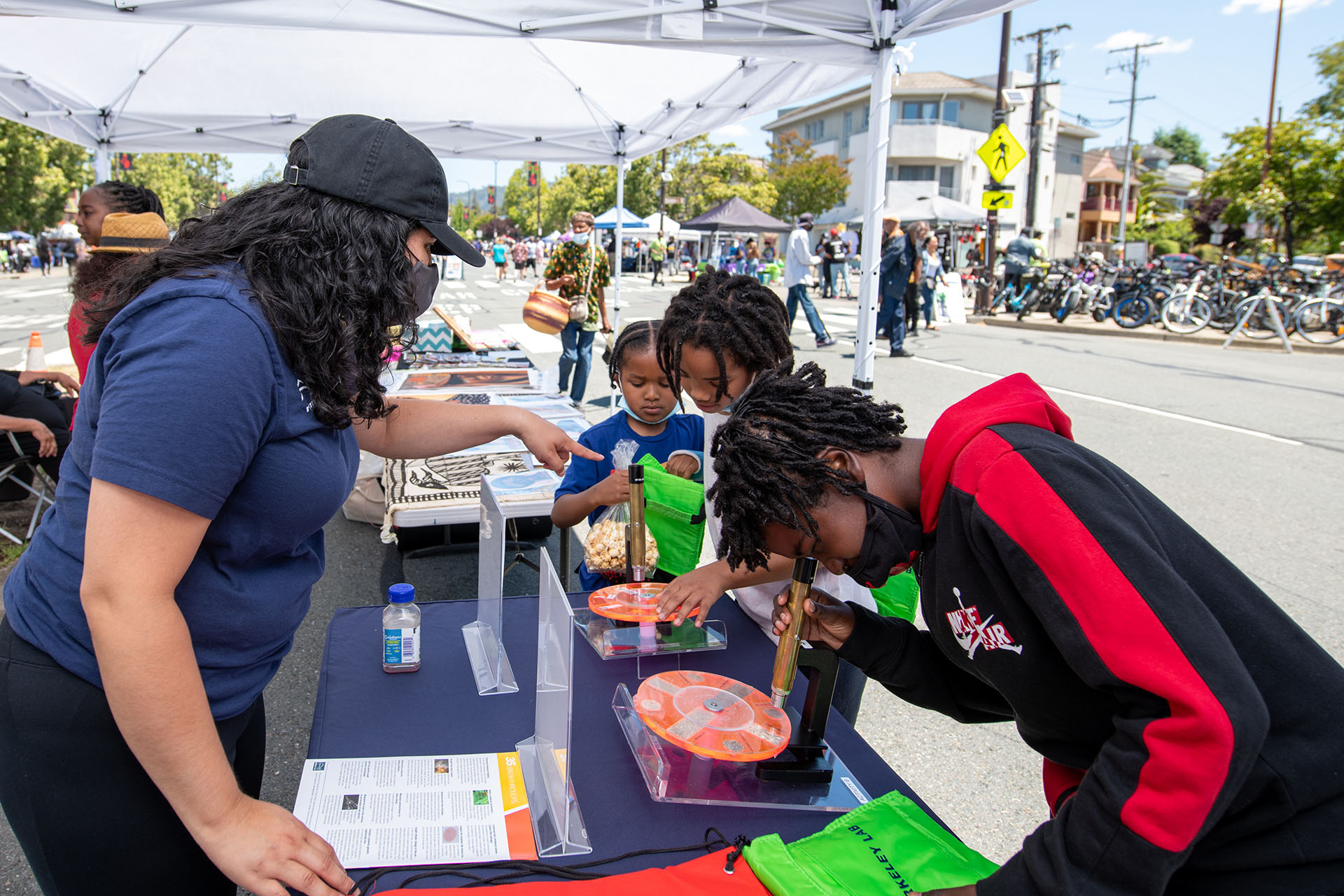 Volunteer shows (left to right) Mali, Kailyal, and Karami Turner how to use the microscope and other hand-on exhibits.