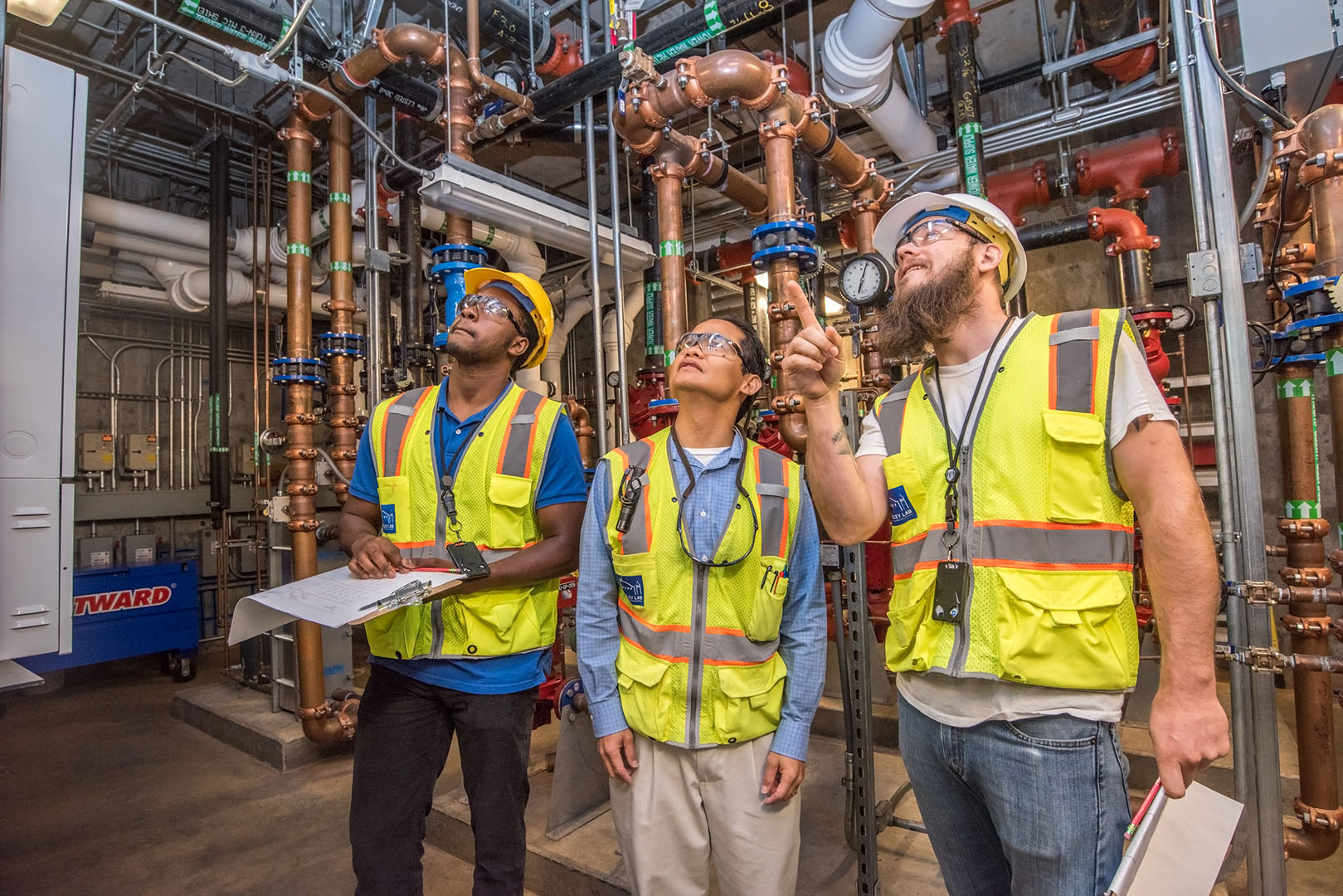 Three people in safety vests look up as they examine facilities.