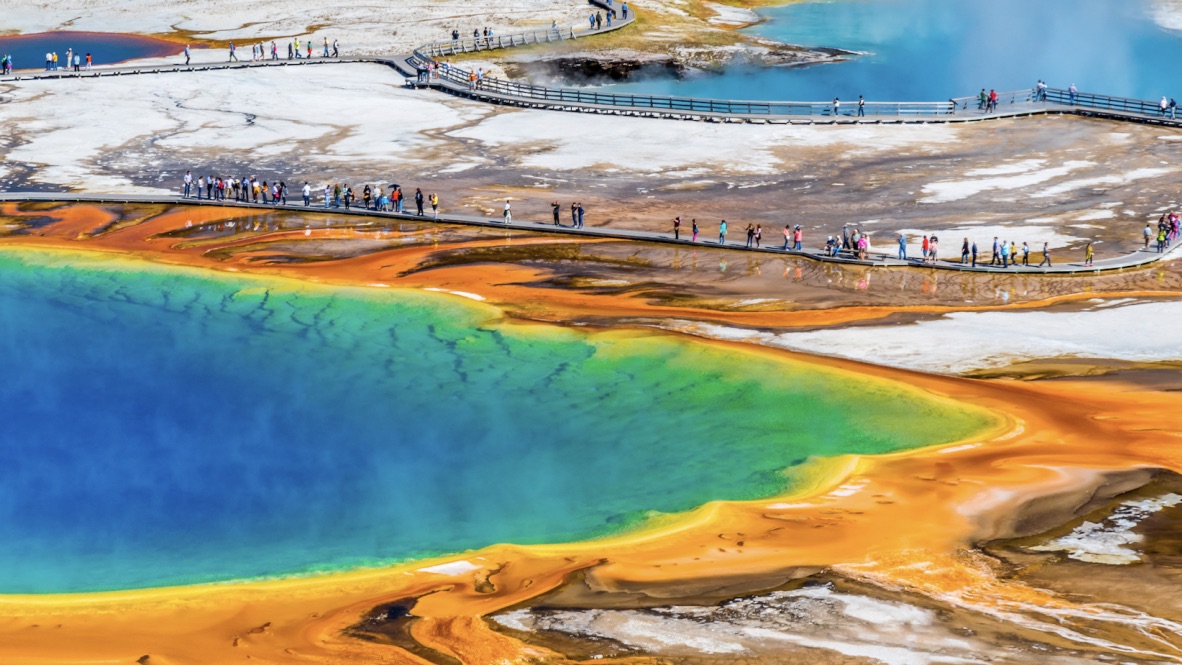 Aerial view of people walking around colorful geothermal pools.