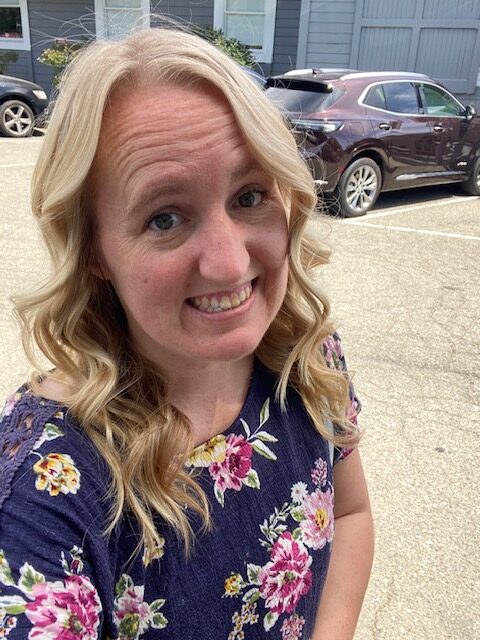 Jessica Porter, a blonde-haired person wearing a floral blouse, smiles for a headshot.
