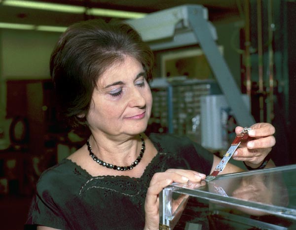 Angelina Galtieri, a dark-haired woman wearing a green blouse and a black necklace, examines an electronic package at her lab.