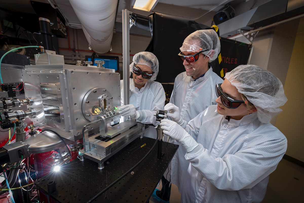 Three scientists work on a large piece of scientific instrumentation.