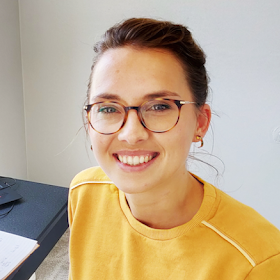 Lieselotte Obst-Huebl, a dark-haired person wearing glasses and a yellow sweater, poses for a headshot.