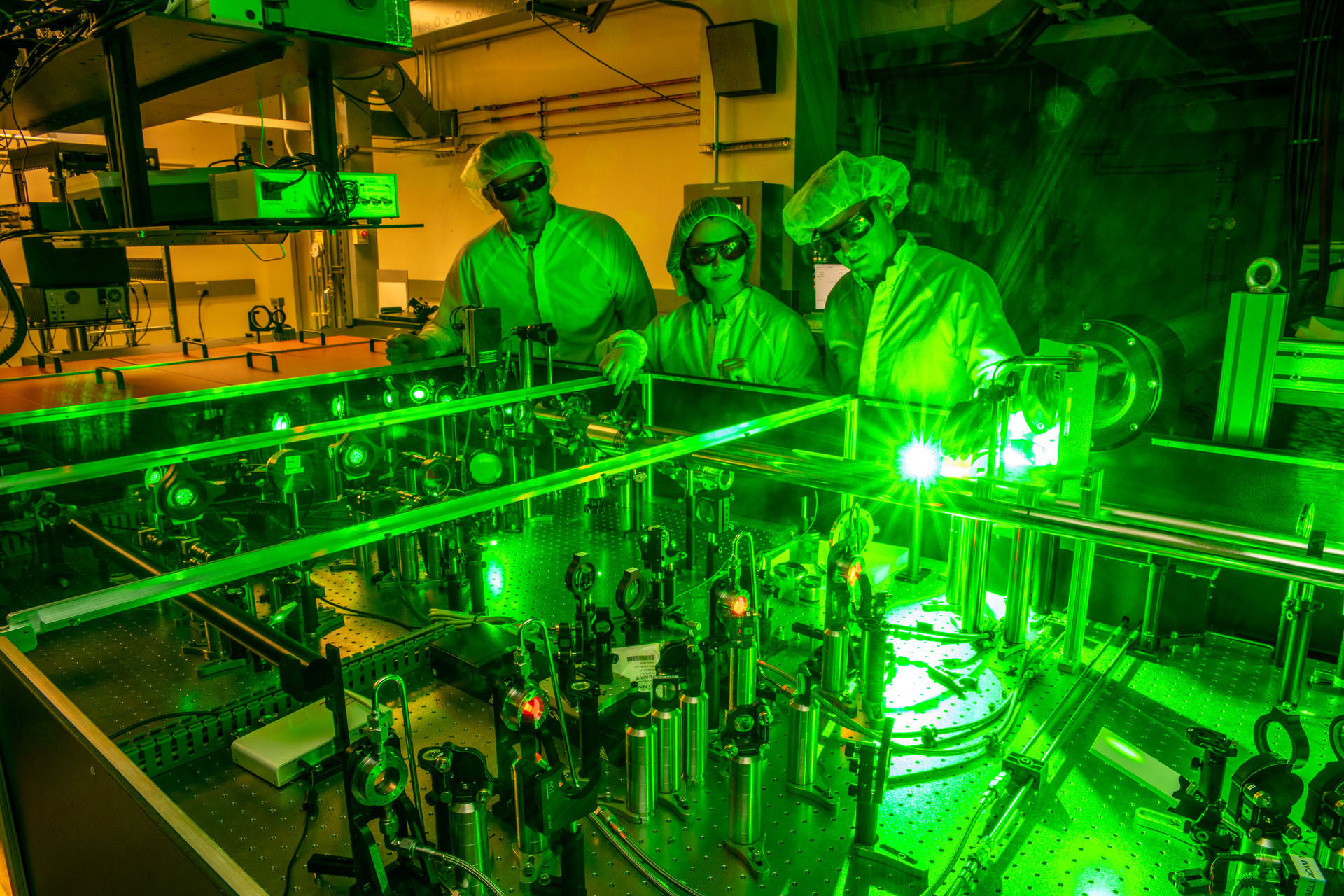 Three scientists looking at a large glowing laser table.