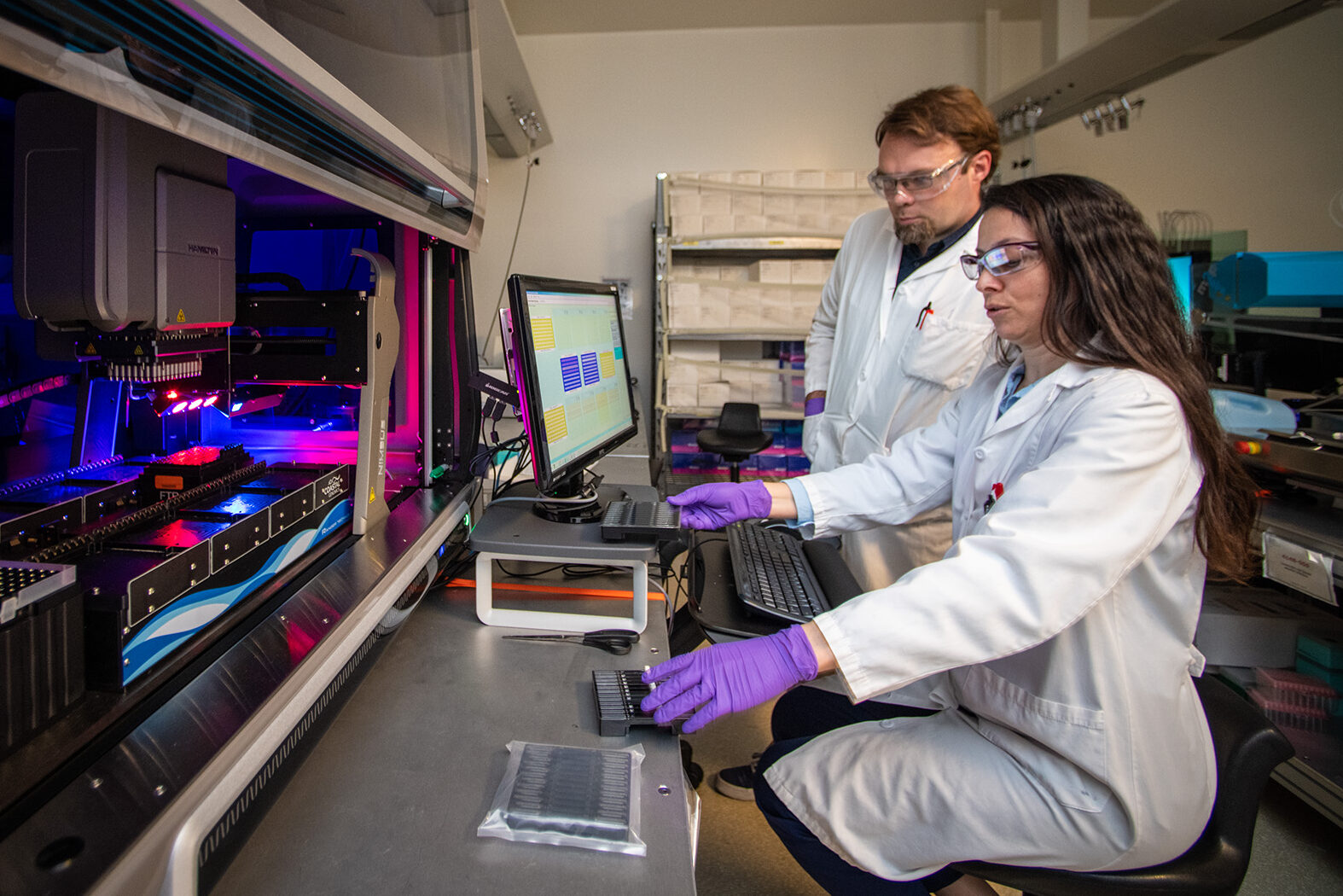 Nurgul Kaplan (front) and Tad Ogorzalek work in the Robots Room on DNA construction and robotics at the Agile BioFoundry.