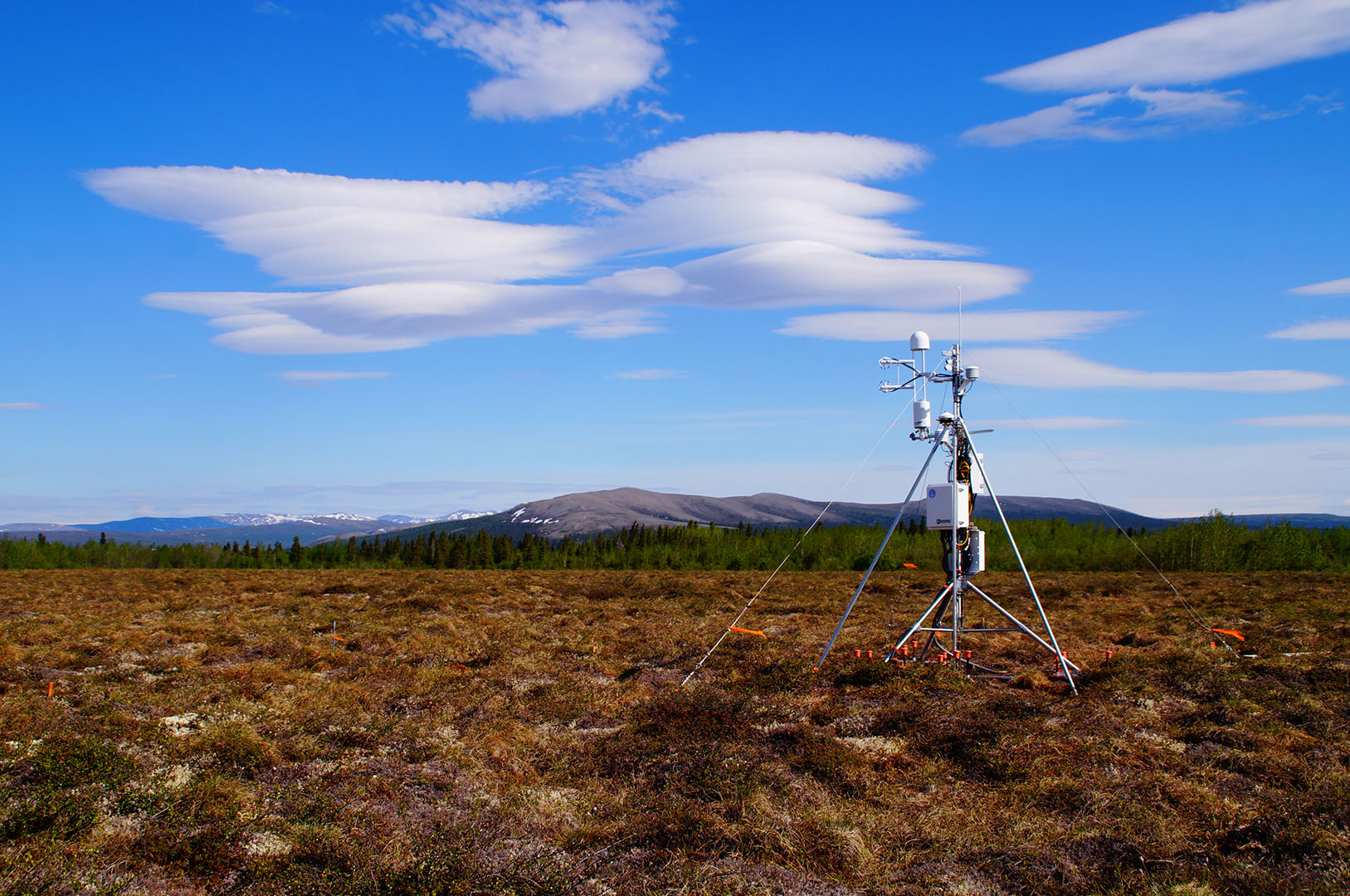 A flux tower in a brown field with clouds above.