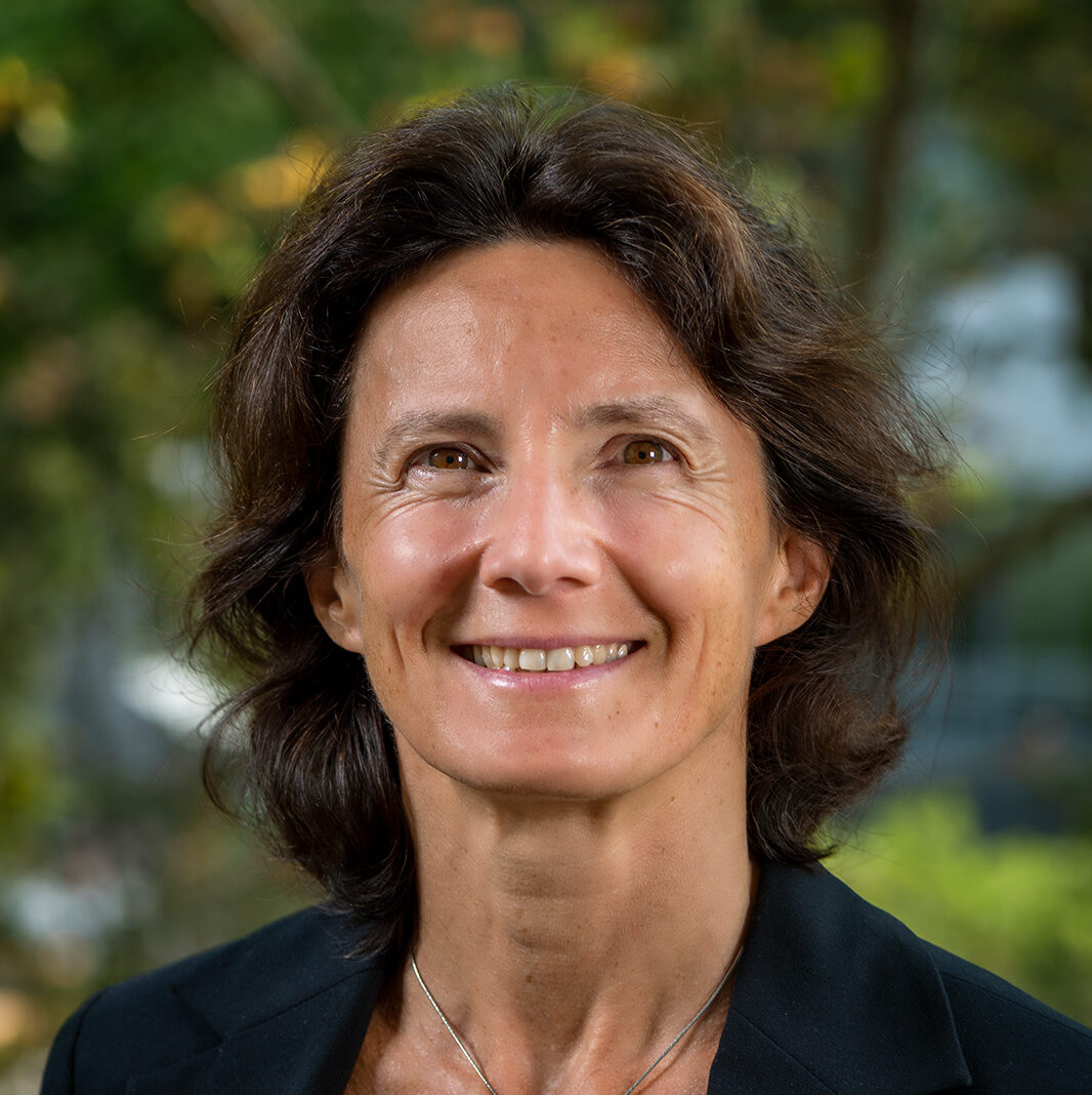 Nathalie Palanque, a dark-haired person wearing a black jackets, smiles for a headshot outdoors.