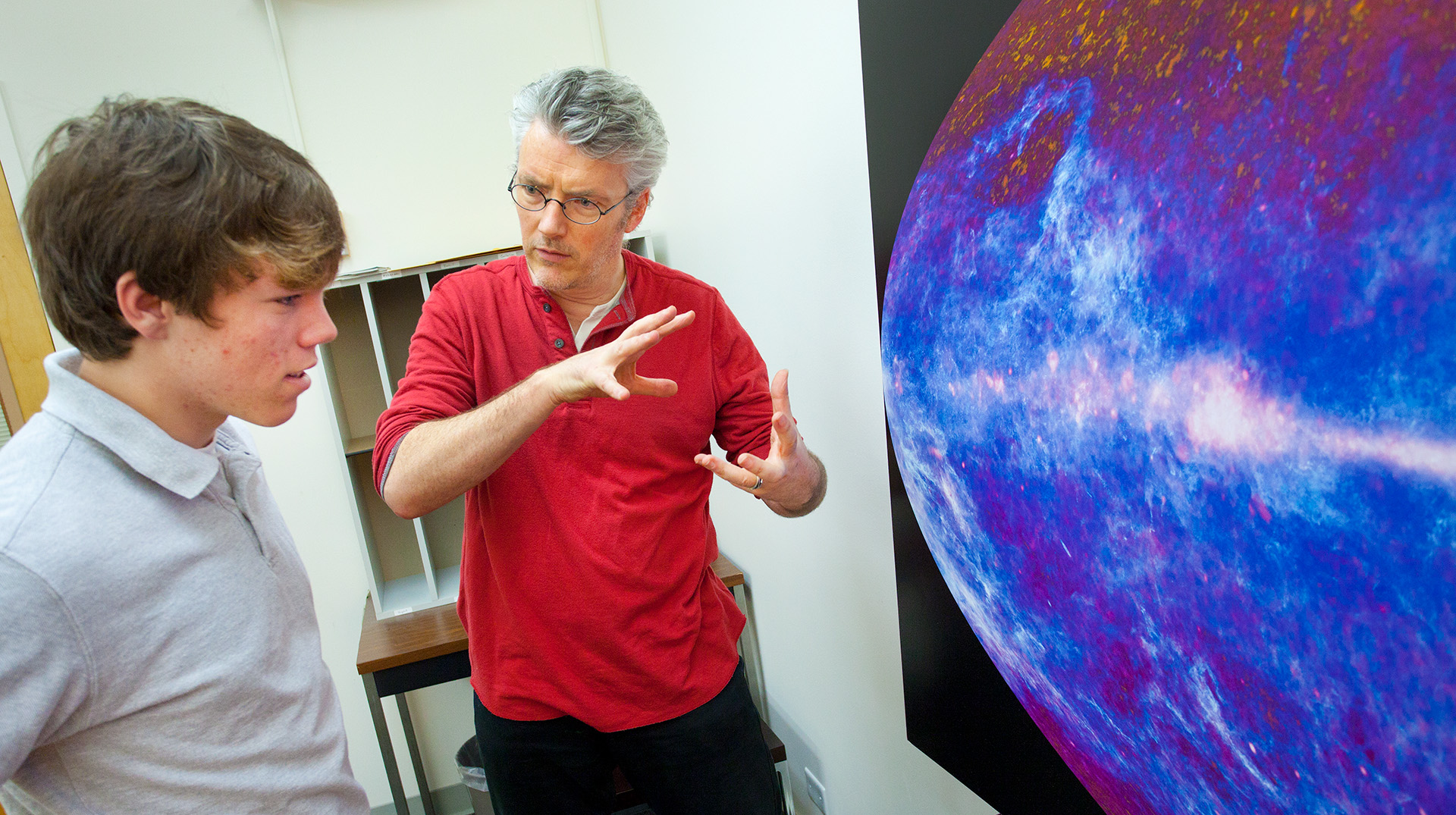 Scientist and student stand in front of a cosmic poster.