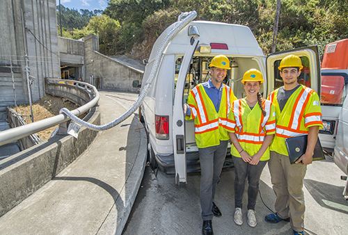 Three people in safety gear standing in front of a truck.