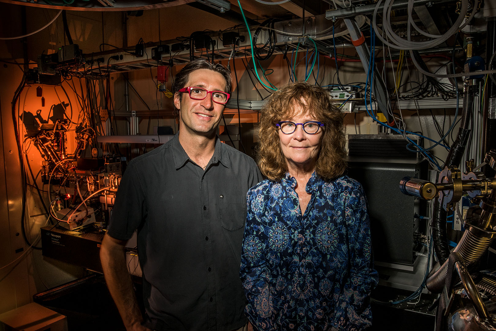 Two scientists posing in front of a dark, wire-filled lab.