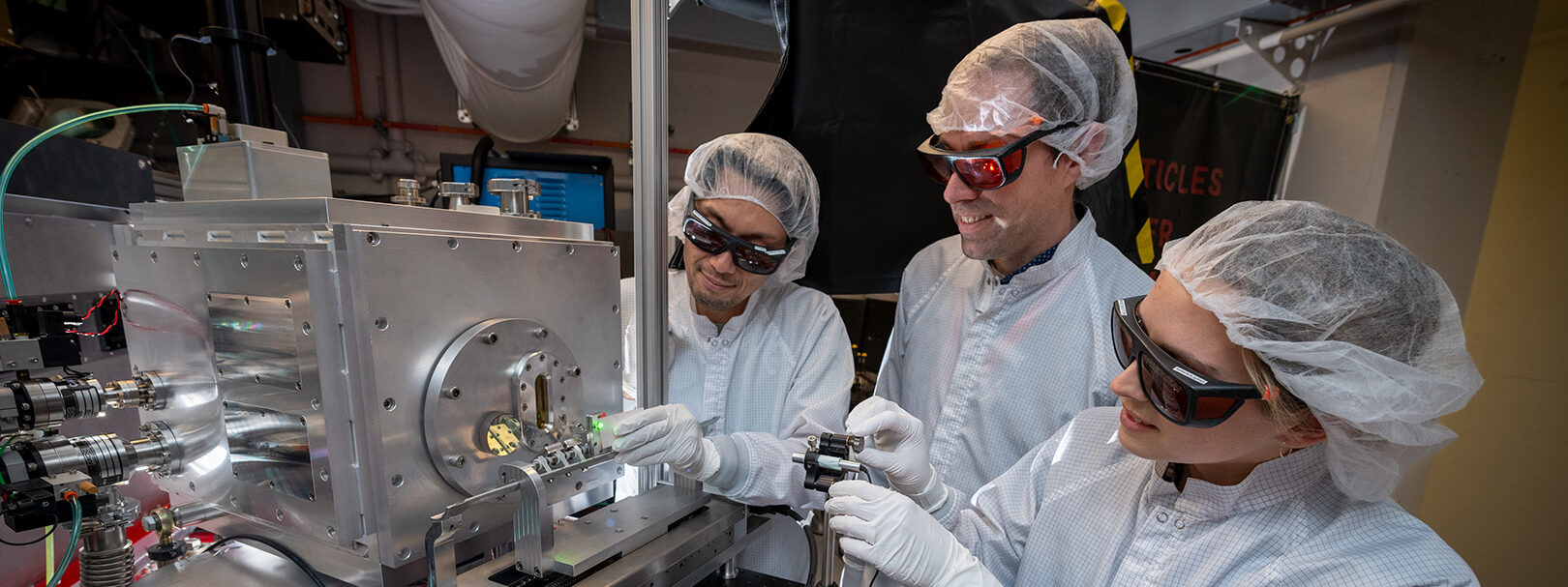 Three scientists adjust a Cell Cartridge Inserter at the end of the BELLA PW Proton Beam LINE at the Berkeley Lab Laser Accelerator.