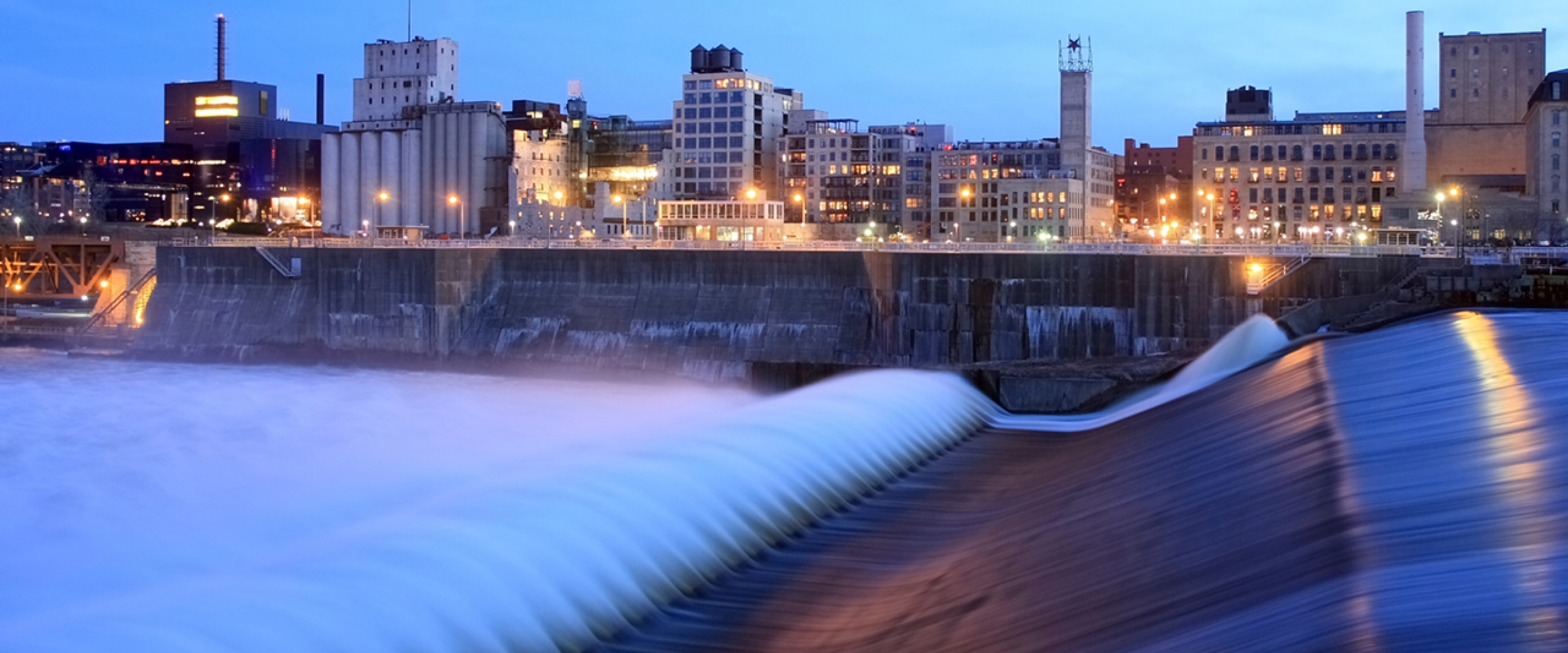 Water dam in front of lit cityscape.