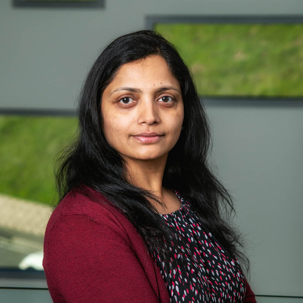 Sumanjeet Kaur, a dark-haired person wearing a red sweater, poses for a headshot.