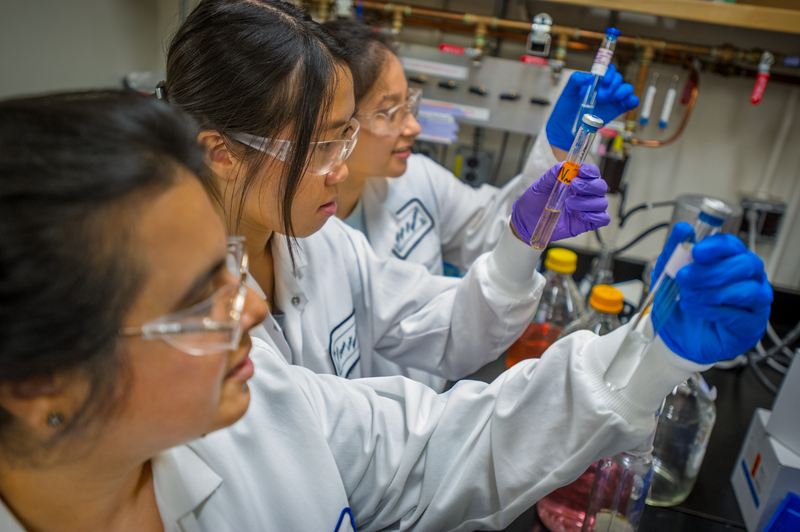 Scientist and two students in a bioscience lab with glass bioreactors.