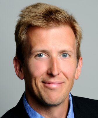 Thomas Kirchstetter, a light-haired person wearing a black suit, smiles for a headshot.