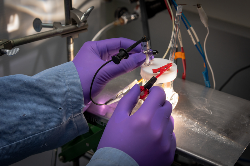 Gloved hands connect wires to an artificial photosynthesis device