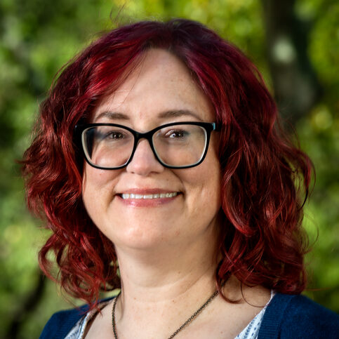 Red-haired person wearing a necklace and a blue top.