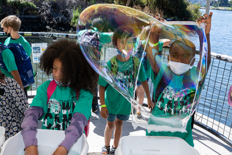 Group of children in green shirts playing with large bubbles.