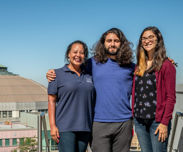 Three people posing outside of a building with a dome-shaped roof.